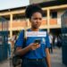 Jovem negra de uniforme azul lê mensagem no celular informando bloqueio temporário do benefício escolar