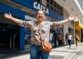 Mulher sorridente celebra em frente à agência da Caixa Econômica.