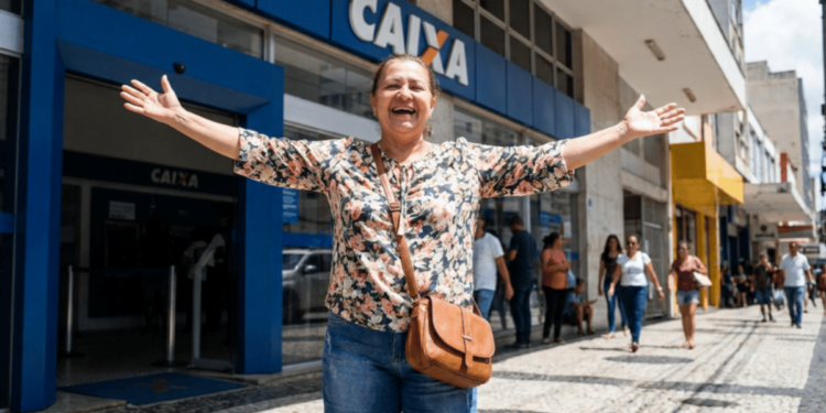Mulher sorridente celebra em frente à agência da Caixa Econômica.