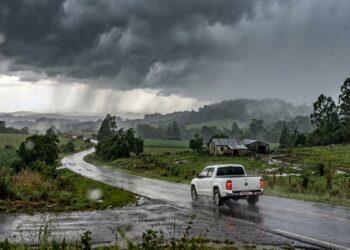 Caminhonete branca trafega por estrada rural sob chuva forte e céu escuro