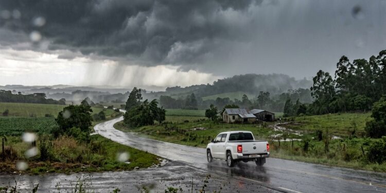 Caminhonete branca trafega por estrada rural sob chuva forte e céu escuro