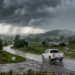 Caminhonete branca trafega por estrada rural sob chuva forte e céu escuro