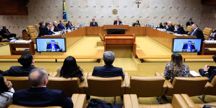Ministros do STF sentados em sessão plenária, com telões exibindo autoridade discursando