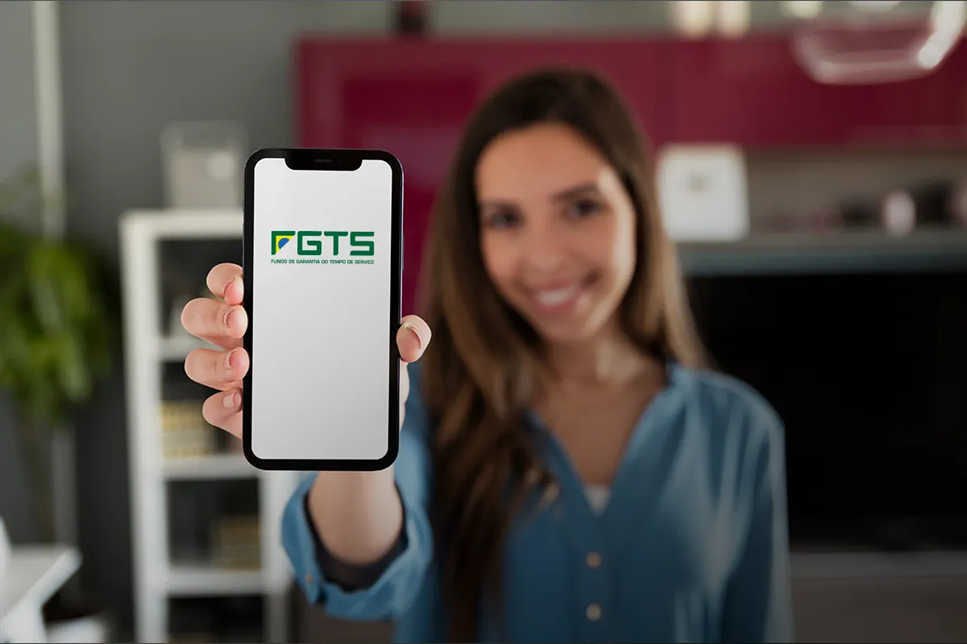 Mulher sorrindo exibe celular com o logo do FGTS no aplicativo em ambiente doméstico