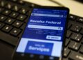 Smartphone exibindo site da Receita Federal sobre teclado preto em ambiente de trabalho