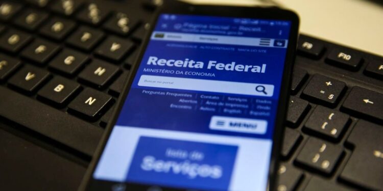 Smartphone exibindo site da Receita Federal sobre teclado preto em ambiente de trabalho