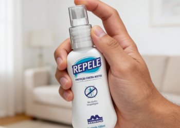 Mão segurando frasco do repelente REPELE com rótulo azul em sala iluminada.