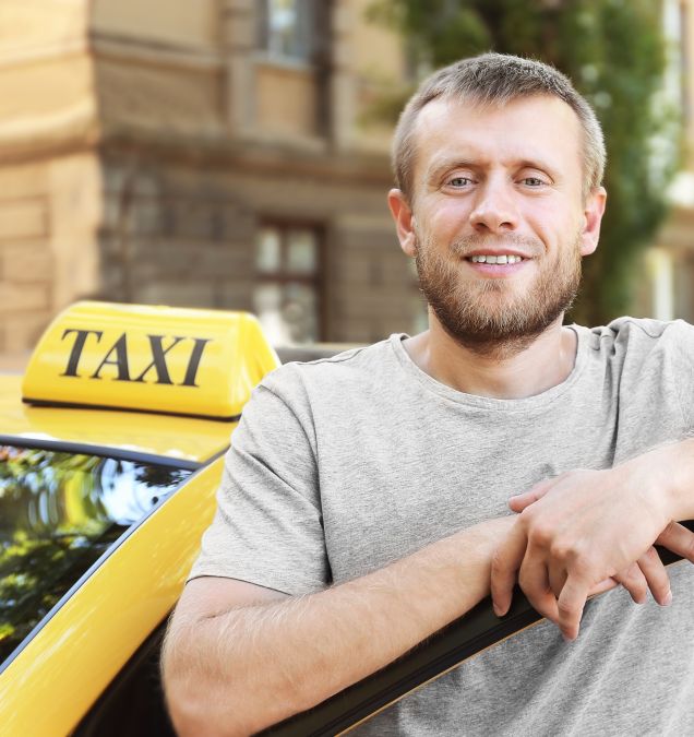 Motorista de táxi sorridente ao lado de veículo amarelo em área urbana.