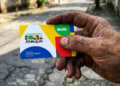 Mão suja exibe cartão do Bolsa Família em rua simples do Brasil.