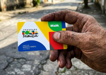 Mão suja exibe cartão do Bolsa Família em rua simples do Brasil.