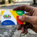 Mão suja exibe cartão do Bolsa Família em rua simples do Brasil.