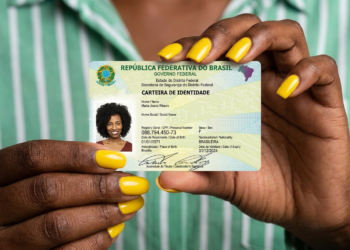Mãos femininas com unhas amarelas segurando Carteira de Identidade Nacional do Distrito Federal com foto de mulher.