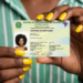 Mãos femininas com unhas amarelas segurando Carteira de Identidade Nacional do Distrito Federal com foto de mulher.
