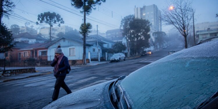 Carro coberto de geada e pedestre agasalhado em rua de serra ilustram a queda de temperatura no Sul após o Inmet descartar ciclone bomba