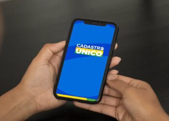 Pessoa segura o celular com a tela do aplicativo do Cadastro Único, sistema que ficará indisponível de quinta a segunda.