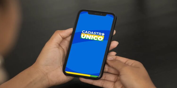 Pessoa segura o celular com a tela do aplicativo do Cadastro Único, sistema que ficará indisponível de quinta a segunda.