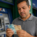 Homem confere notas de cem e cinquenta reais em frente a caixa eletrônico da Caixa