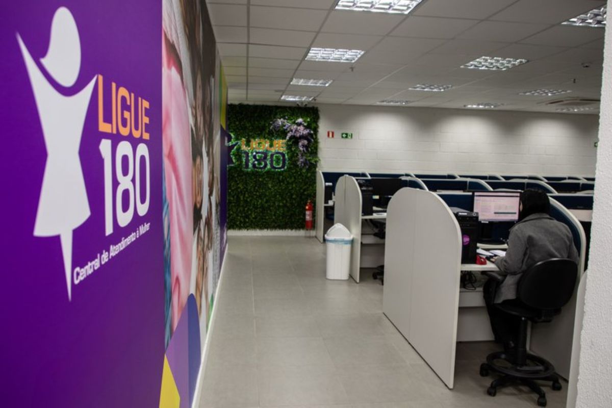 Central de atendimento Ligue 180 com painel da campanha e atendente em estação de trabalho