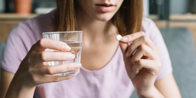 Mulher segura comprimido e copo com água, representando medicamento oral aprovado pela Anvisa para câncer de mama.