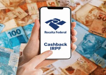 Mão segura celular com a marca da Receita Federal e o texto Cashback IRPF, sobre fundo de cédulas de real