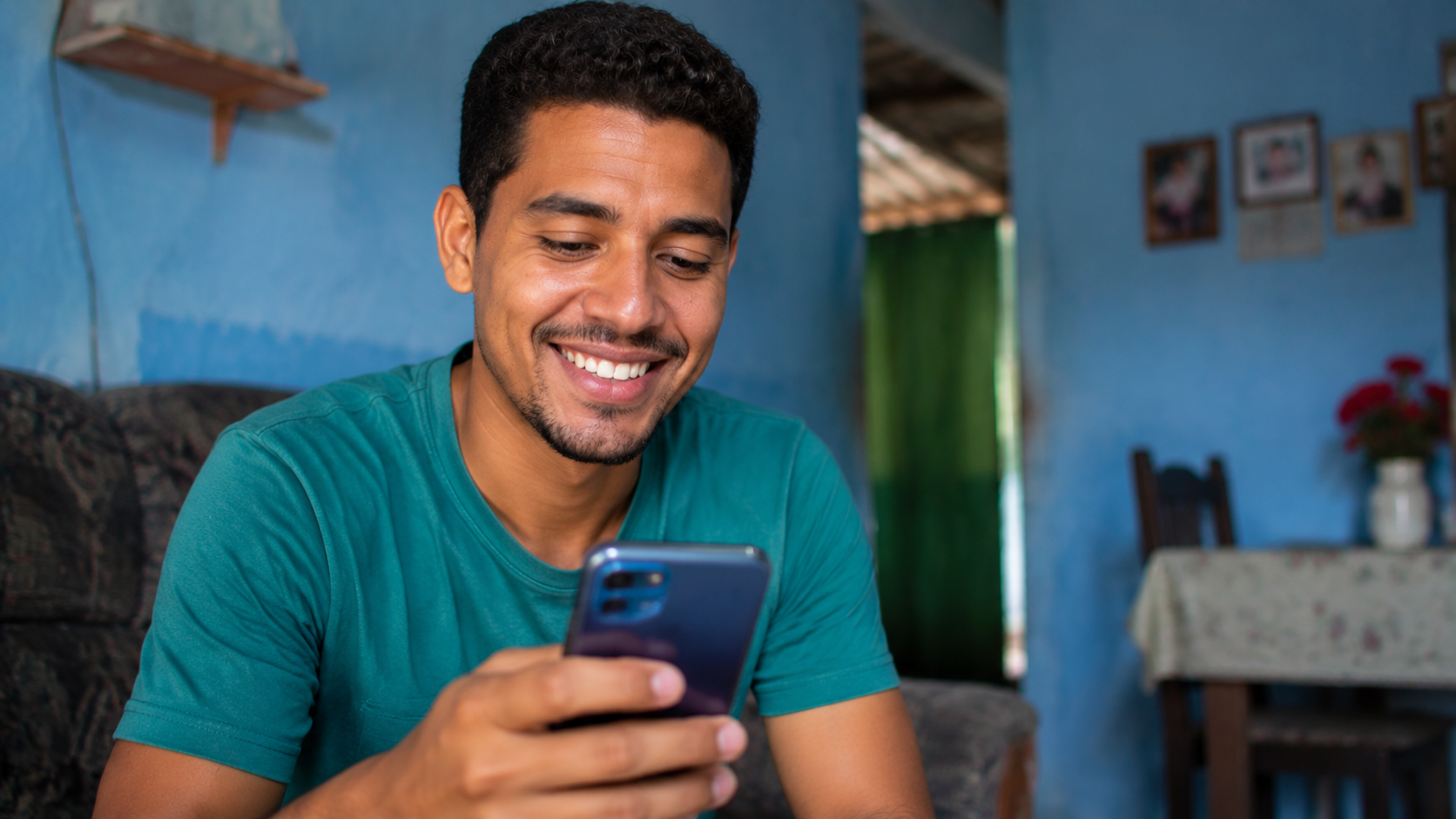 Homem jovem sorrindo enquanto usa o celular em casa, em referência à consulta e à inscrição no Programa Acredita no Primeiro Passo por meio do CadÚnico