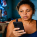 Beneficiária consulta o celular com atenção dentro de casa
