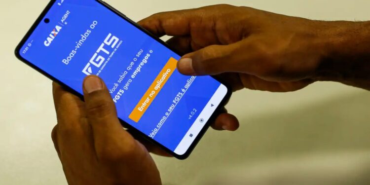 Pessoa segura o celular com o aplicativo do FGTS da Caixa aberto, em referência ao uso do fundo como garantia no Consignado CLT