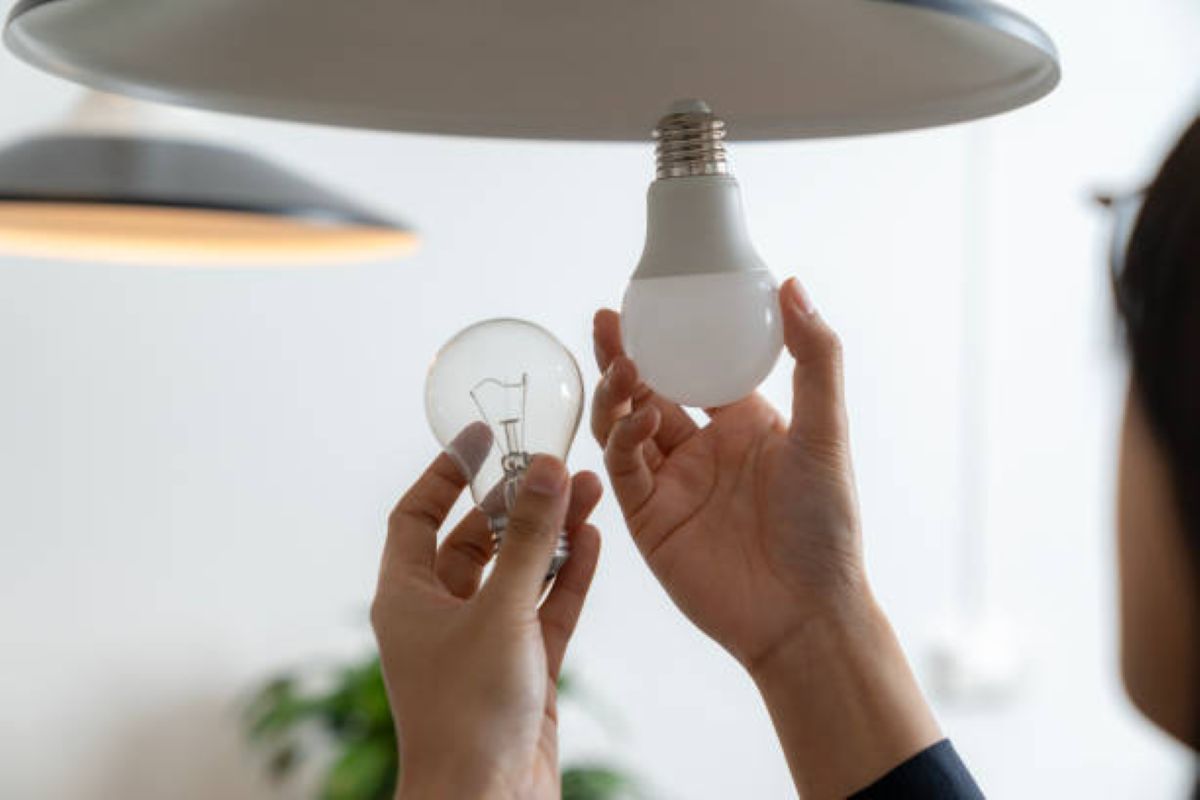 Mulher troca lâmpada incandescente por modelo de LED em luminária do teto