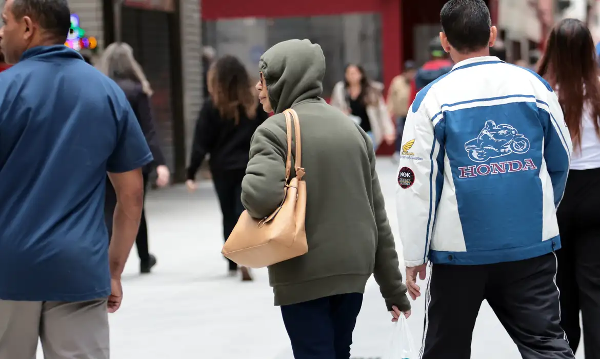 Pedestres de casaco e capuz caminham na rua durante a frente fria que reduz as temperaturas no Sul