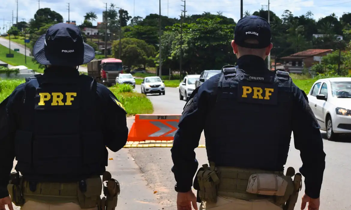 Policiais rodoviários federais de costas em uma rodovia, em referência ao órgão cujo nome é usado por golpistas.