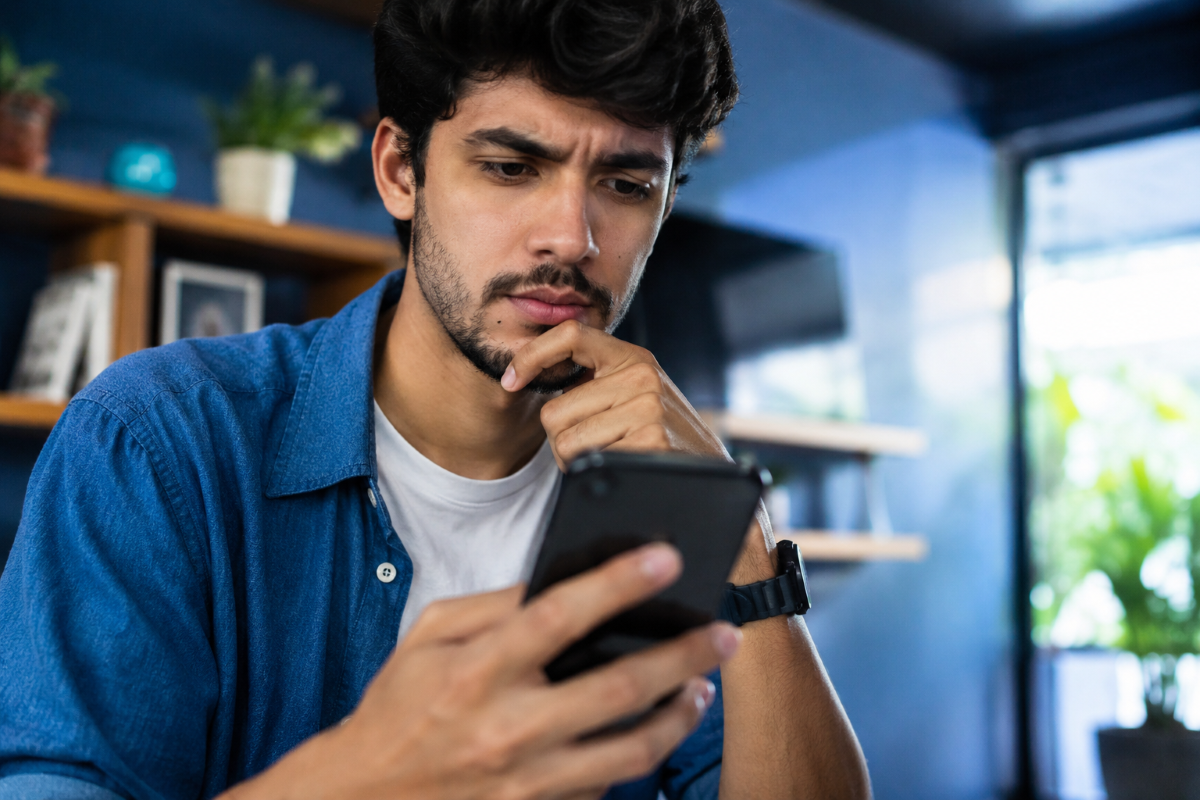 Homem concentrado consulta o celular em casa enquanto verifica processo de recuperação de conta