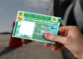 Mão segura a Carteira Nacional de Habilitação ao lado de um carro, documento que agora pode ser renovado gratuitamente por bons condutores