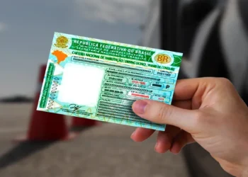 Mão segura a Carteira Nacional de Habilitação ao lado de um carro, documento que agora pode ser renovado gratuitamente por bons condutores