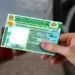 Mão segura a Carteira Nacional de Habilitação ao lado de um carro, documento que agora pode ser renovado gratuitamente por bons condutores