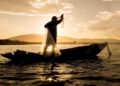 Pescador lança rede de pesca em barco ao pôr do sol em rio brasileiro