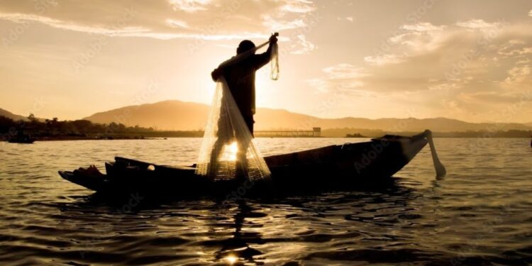 Pescador lança rede de pesca em barco ao pôr do sol em rio brasileiro