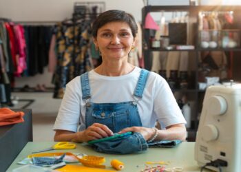 Costureira sorri em seu ateliê, ao lado da máquina de costura, tesoura e fita métrica, perfil de microempreendedora individual que seria beneficiada pelo novo teto do MEI