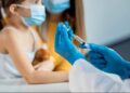 Profissional de saúde com luvas azuis prepara seringa para vacinação infantil