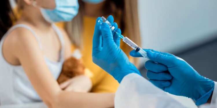 Profissional de saúde com luvas azuis prepara seringa para vacinação infantil