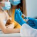 Profissional de saúde com luvas azuis prepara seringa para vacinação infantil