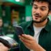 Homem paga aproximando o celular da maquininha; modalidade perde o limite de R$ 500 com a nova regra do Banco Central