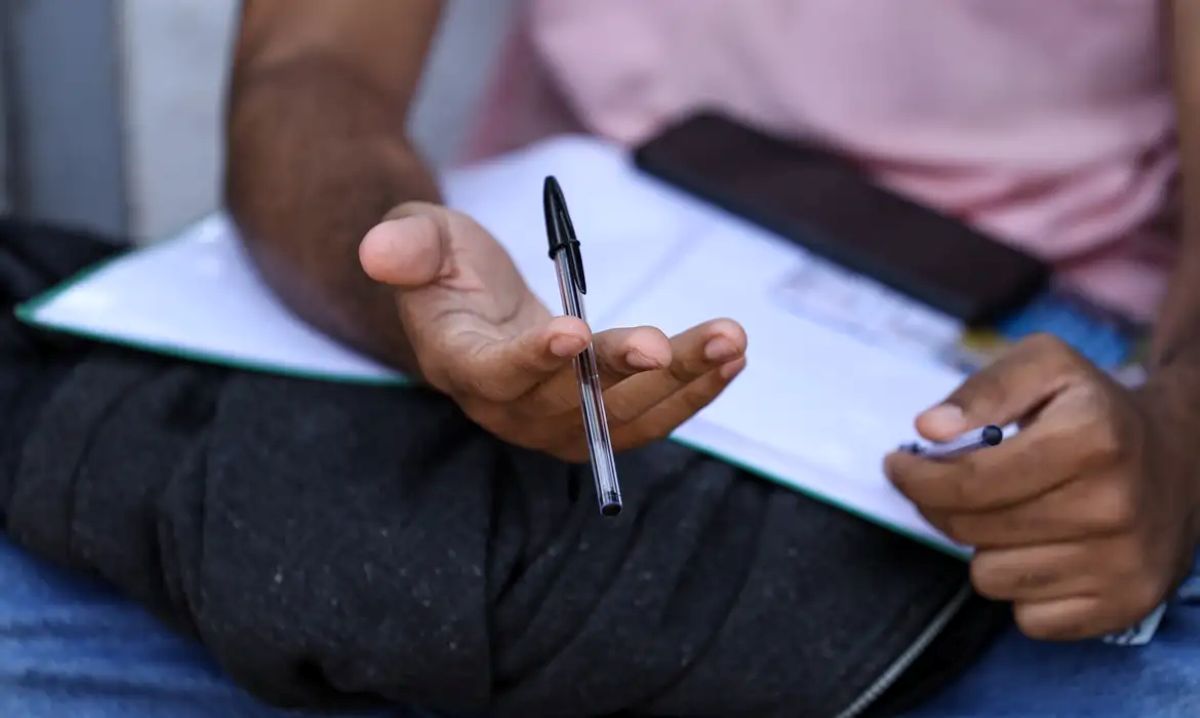 Estudante segura caneta preta sobre caderno aberto enquanto estuda em close das mãos