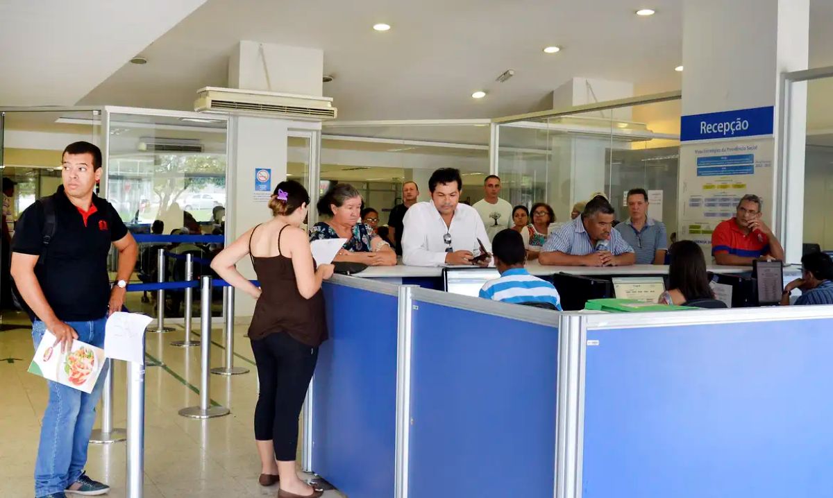 Pessoas aguardam atendimento na recepção de agência do INSS em fila e balcão
