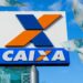 Imagem ilustrativa com a placa do logotipo da Caixa Econômica Federal cercada por cédulas de cem reais, em referência ao pagamento do Bolsa Família.
