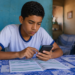 Estudante de uniforme consulta o celular com documento sobre a mesa em casa