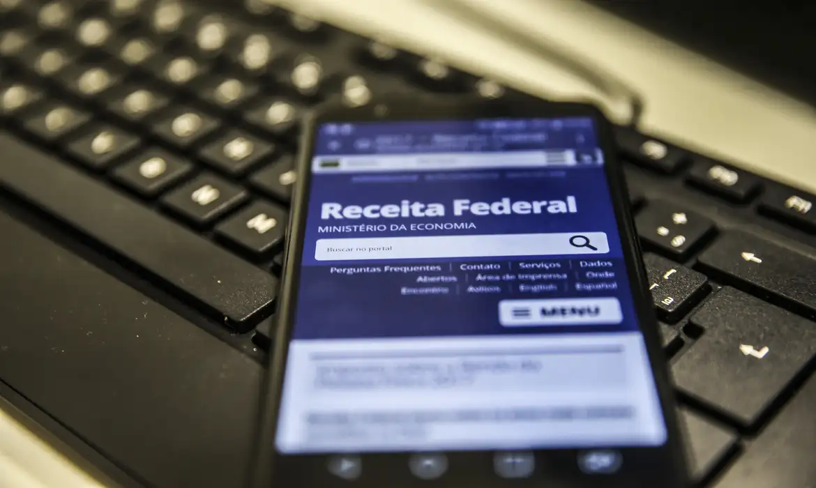 Celular exibindo o site da Receita Federal sobre um teclado, representando a mudança do CNPJ para o formato alfanumérico.