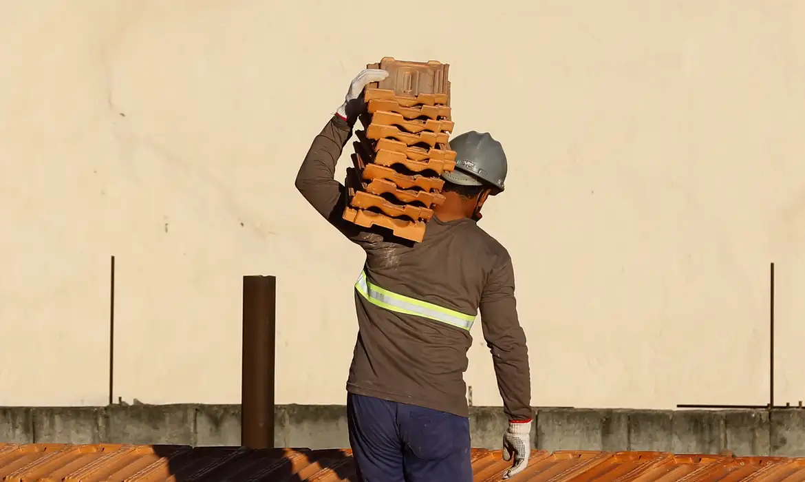 Operário carrega telhas no ombro em uma obra, representando as reformas financiadas pelo Reforma Casa Brasil com juros baixos.