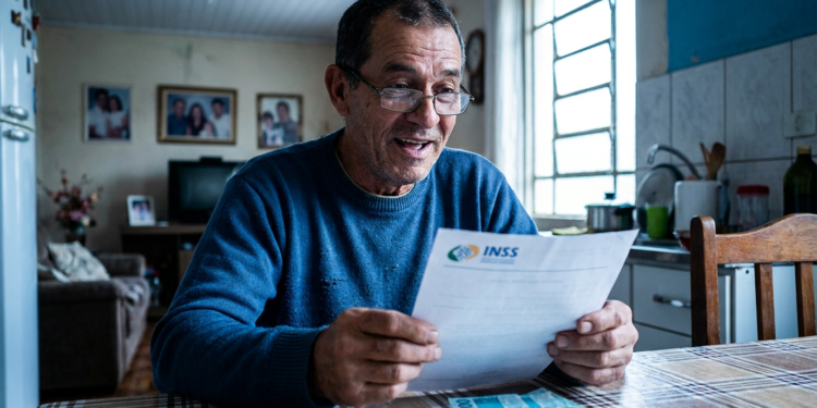 Aposentado confere documento do INSS em casa, verificando descontos para pedir o ressarcimento.