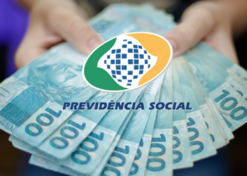 Mãos segurando notas de 100 reais em leque sob logo da Previdência Social do Brasil.