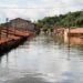 Casas com telhados vermelhos submersas por enchente em rua alagada, céu parcialmente nublado